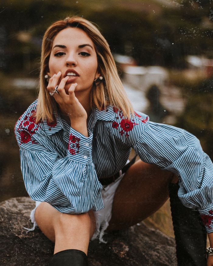 Portrait of a stylish woman sitting on a rock, wearing embroidered attire in Catamarca, Argentina.