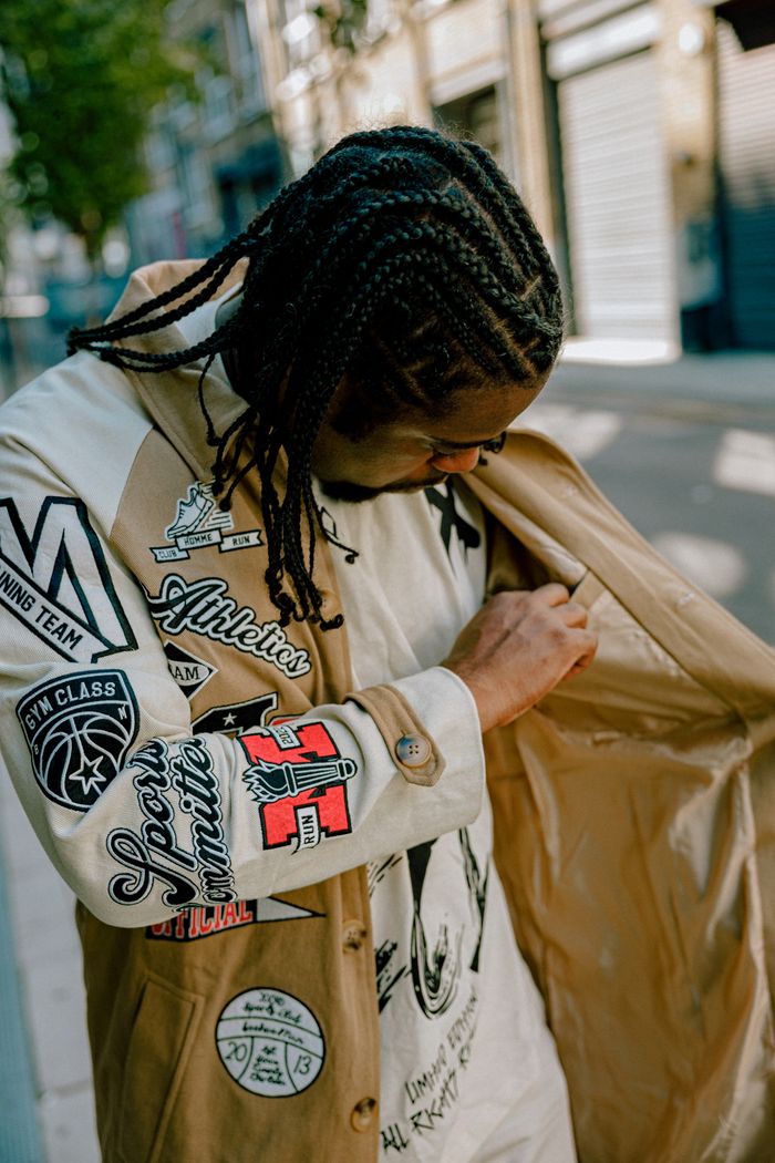 Man with braided hair inspecting jacket with patches on sunny street.