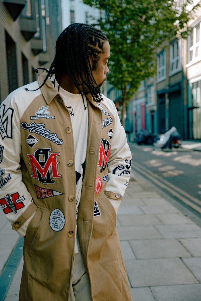 A fashionable person with braided hair in a stylish coat on a city sidewalk.