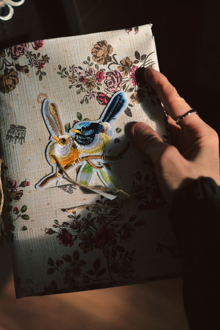 A hand holding a floral-covered notebook with embroidery, in soft lighting.
